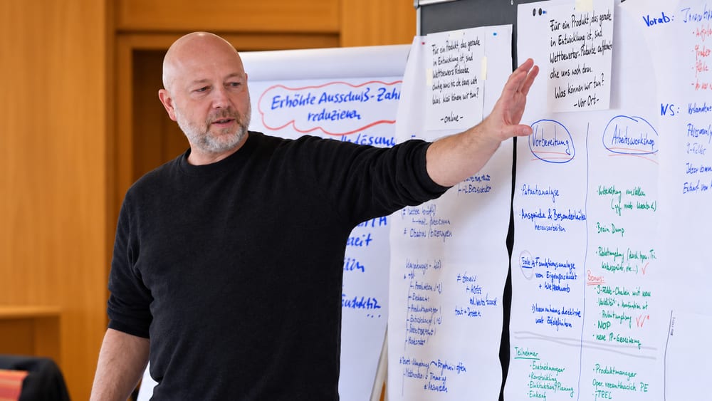 Gregor Panitz bei der Entwicklungsarbeit mit einem Team – erklärt an Flipcharts ein technisches Problem